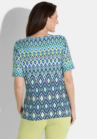 Top à manches courtes avec un motif géométrique en diamants dans les tons bleu, vert et marine, fabriqué dans un tissu léger. Encolure ronde simple.