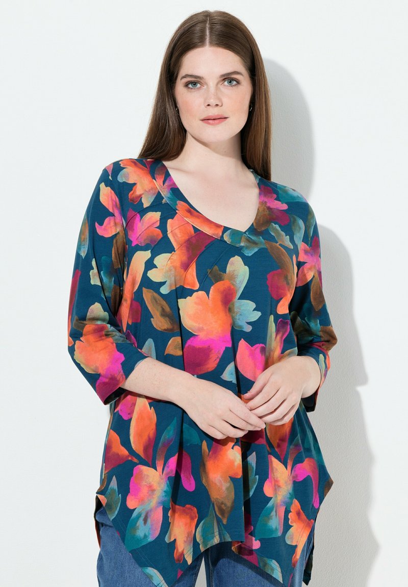 Mehrfarbige florale Tunika mit dreiviertellangen Ärmeln, tiefem V-Ausschnitt und fließendem Design. Hauptfarben: Türkis, Rosa, Orange und Grün.