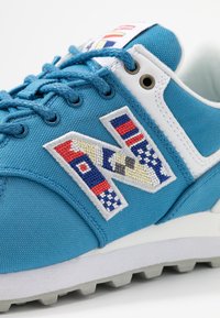 Baskets en tissu bleu avec un logo "N" brodé en blanc, des motifs colorés et une surface texturée. Présente des accents blancs et une semelle grise.