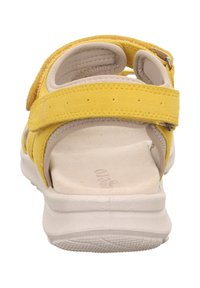 Żółta sandałka zamszowa z regulowanymi paskami na rzep, wyściełaną wkładką i białą gumową podeszwą z teksturowaną powierzchnią dla lepszej przyczepności.