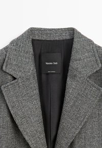 Szary żakiet z wełny z domieszką, z teksturowanym materiałem, klapami i czarną podszewką. Zawiera metkę z napisem "Massimo Dutti" wewnątrz kołnierza.