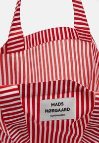 Czerwono-biała torba na ramię w paski z mocnymi uchwytami, z etykietą „MADS NØRGAARD COPENHAGEN” wyszytą wewnątrz.