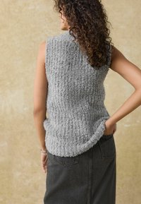 Top de punto gris sin mangas con textura y un dobladillo ligeramente curvado, combinado con una falda de mezclilla oscura que cuenta con bolsillos y una silueta ajustada.