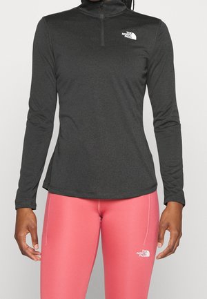 Personne portant un pull à manches longues North Face gris foncé avec une fermeture éclair quart et des leggings North Face rose vif.