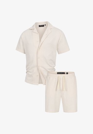 Lyhytselkäinen nappikauluspaita ja yhteensopivat shortsit vaaleassa kermassa, joissa on hienovaraiset pystysuorat raidat. Ominaisuuksiin kuuluu rento leikkaus ja nyöri vyötäröllä.