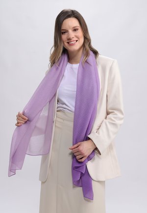 Écharpe en lavande à côtes, fabriquée dans un matériau léger et transparent, drapée autour des épaules. Portée avec un blazer crème et un haut blanc.