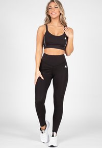Zwart atletisch crop-top met dunne banden en witte accenten, gecombineerd met hoge zwarte leggings met een logo. Gecombineerd met witte sneakers.