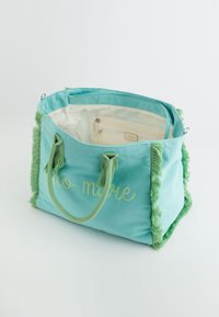 Canvas tote bag in teal met groene franjesaccenten. Heeft een beige voering en een binnenzak. Tekst "ciao amore" geborduurd op de voorkant.