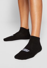 Chaussettes basses noires en tissu texturé, avec un logo blanc sur le côté. Le design comprend des sections côtelées pour un meilleur maintien.