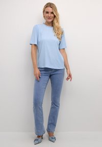 Blusa azzurro chiaro a maniche corte con modello testurizzato e scollatura arricciata, abbinata a jeans a palazzo azzurro chiaro e scarpe con accentuazione a fiocco.