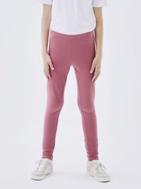 Leggings en coton rose avec une coupe ajustée et une taille élastique, présentant une texture lisse et des coutures minimales. Associés à des baskets blanches.
