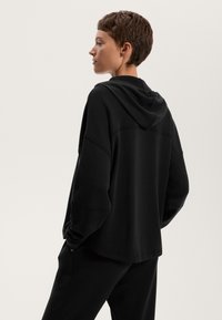 Fekete kapucnis pulóver laza szabással, húzózsinóros kapucnival és lelógó vállvarrással. Puha anyagból készült, sima felülettel.