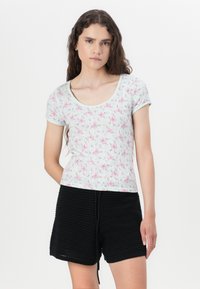 Top floreale a maniche corte in azzurro chiaro con fiori rosa e strisce orizzontali; abbinato a pantaloni corti neri a trama con coulisse.
