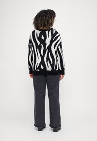 Μαύρο και λευκό πουλόβερ με ρίγες zebra, σε χαλαρή γραμμή, με ριμπ μανσέτες και ψηλό λαιμό, συνδυασμένο με σκούρες γκρι παντελόνες σε φαρδιά γραμμή.