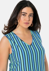 Ärmlös v-ringad topp i ljusblå och gröna ränder med svarta detaljer. Mjuk tyg; har en avslappnad passform och sidoseamsdetaljer.