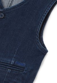 Marineblauer Jeanswesten mit einem einzigen Knopf, ausgestattet mit einer dekorativen Tasche und einem kleinen Logo-Patch in der Nähe des Saums, mit glatter Textur.