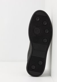 Zwarte rubberen schoenzool met horizontale en verticale ribbels, voorzien van cirkelvormige grip en "HILFIGER" in reliëf aan de zijkant.