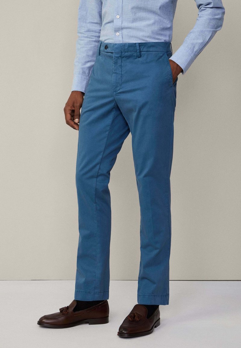 Niebieskie chinosy bawełniane o prostym kroju, z paskiem na błotnikach i kieszeniami bocznymi, zestawione z ciemnobrązowymi loafersami.