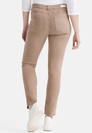 Hellbraune Slim-Fit-Jeans mit Gesäßtaschen und glatter Textur, kombiniert mit weißen Sneakers, von hinten sichtbar.