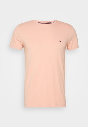Hell pfirsichfarbenes T-Shirt mit kurzen Ärmeln und Rundhalsausschnitt mit kleinem rechteckigem roten, weißen und blauen Logo auf der linken Brust.