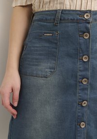 Blue denim skirt with a high waist, front button closure, large side pocket, and faded texture. Features six metallic buttons along the front.