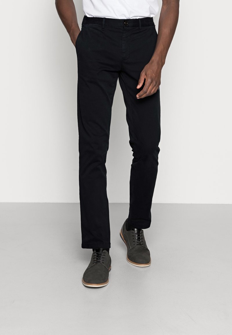 Chinos neri in cotone con design a gamba dritta. Abbinati a scarpe grigio scuro con lacci e suola chiara.