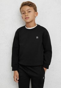 Hanorac negru cu manșete ribbate, guler rotund și logo alb "R" pe piept, asortat cu pantaloni de trening negri.
