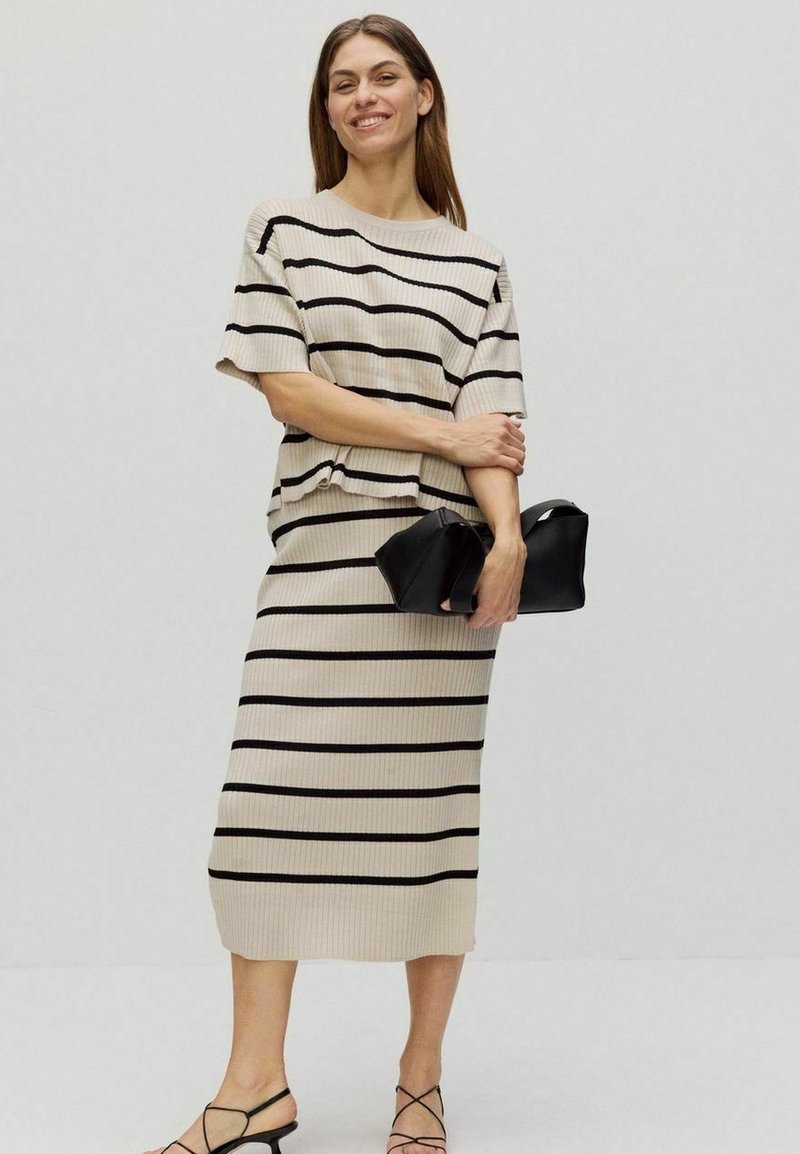 Beige ribbad stickad klänning och toppset med svarta horisontella ränder, med en avslappnad passform och korta ärmar, kompletterat med en svart handväska.