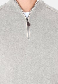 Maglione grigio con zip e colletto alto, dotato di una cerniera e un tirante in pelle. Realizzato in un tessuto morbido con una texture liscia.