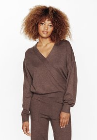 Haut enveloppant en tricot marron avec un décolleté en V, des manches longues et des poignets côtelés, associé à un pantalon marron assorti.
