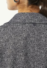 Houndstooth-patterned jacket with a collar. Made of textured fabric in dark blue and white, featuring a button closure at the back neckline.