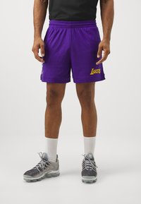 Pantaloni da basket in rete viola con scritta gialla "LAKERS", vita elasticizzata e fessure laterali. Abbinati a scarpe da ginnastica grigie e calze bianche.
