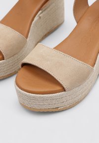 Sandalias de cuña beige con parte superior de ante y plantilla de cuero marrón. Base de plataforma envuelta en yute con detalle de costura visible.