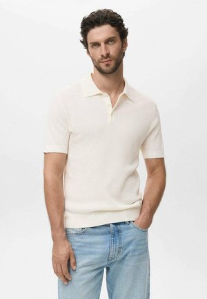Camisa polo de manga corta color crema con textura acanalada, que presenta una tapeta de dos botones y un cuello ligero. Llevada con jeans azul claro.