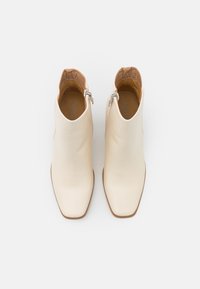 Botas de tobillo de cuero blanco con un diseño elegante, puntera cuadrada y cremallera lateral. Forro texturizado visible en el borde superior.