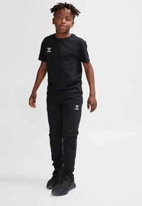 Zwart T-shirt en zwarte broek met logodetail op de linkerborst en zak, gemaakt van een katoenmengsel, gedragen met zwarte sneakers.