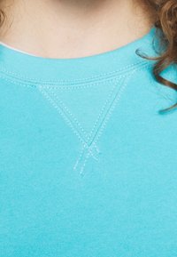 Světlomodrý svetr s texturovaným, prošívaným detailem do tvaru V na výstřihu. Měkká tkanina s hladkým povrchem.