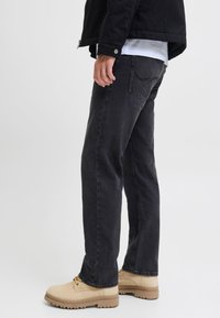 Vaqueros de denim negro con un corte holgado, combinados con botas beige de cordones. La textura es resistente y los vaqueros presentan un detalle mínimo en la parte trasera.