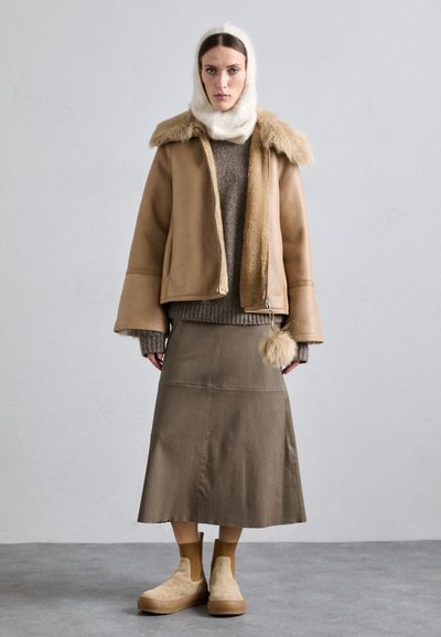 Καφέ δερμάτινο μπουφάν με γούνινο γιακά, γκρι πλεκτό πουλόβερ, καφέ φούστα και μπεζ μποτάκια μέχρι τον αστράγαλο. Σημαντική λεπτομέρεια με γούνινη μπάλα στη φούστα.