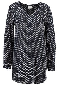 Marineblauwe blouse met lange mouwen en een V-hals, met een repetitief bloemenpatroon in crème en roze, gemaakt van lichte stof met een fijne textuur.