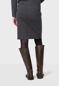 Des bottes en cuir brun montantes avec une semelle plate, associées à une jupe en tricot gris et des collants noirs. La jupe présente un design simple.
