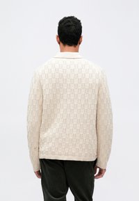 Lys beige, strukturrert strikk cardigan med ribbete krage og mansjetter, med en vanlig passform og subtilt mønster gjennom hele.