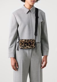 Leopard print crossbody bag with a soft texture, black accents, and adjustable strap. The bag features a zip closure and side tassels.