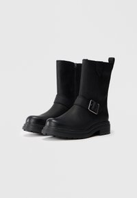 Black ankle boots made of leather, featuring a side zipper, a strap with a buckle detail, and a thick, textured sole.