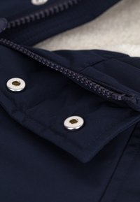 Marineblaue isolierte Jacke mit glatter Außenfläche, silbernen Druckknöpfen und einem robusten Reißverschluss vorne zur Schließung.