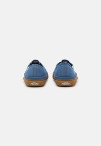 Sapatos slip-on em lona azul com uma superfície texturizada, solas de borracha castanha clara e um logo "Vans Off the Wall" no calcanhar.