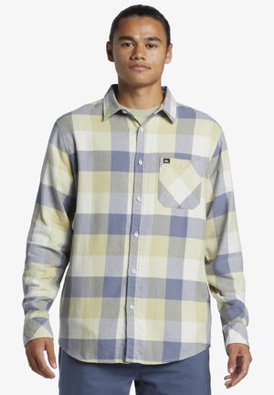 Long-sleeve, button-up plaid shirt featuring large yellow, green, and blue squares, with a chest pocket and a soft, textured fabric.