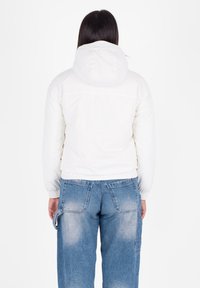 Witte pufferjas met een capuchon, elastische manchetten en een cropped pasvorm. Gemaakt met lichtblauwe losse jeans met een vervaagde textuur en zakken.