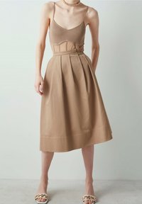 Beige midi-jurk met een aansluitend geribd lijfje en een geplooide rok. Gladde textuur met een subtiele glans. Gecombineerd met witte sandalen en een gouden ketting.