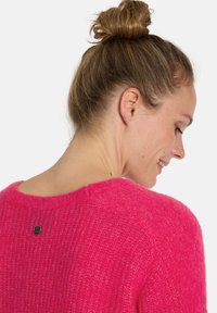 Fuchsia Strickpullover mit lockerer Passform, Rundhalsausschnitt und strukturierter Oberfläche. Mit einem kleinen Metallakzent auf der Rückseite.